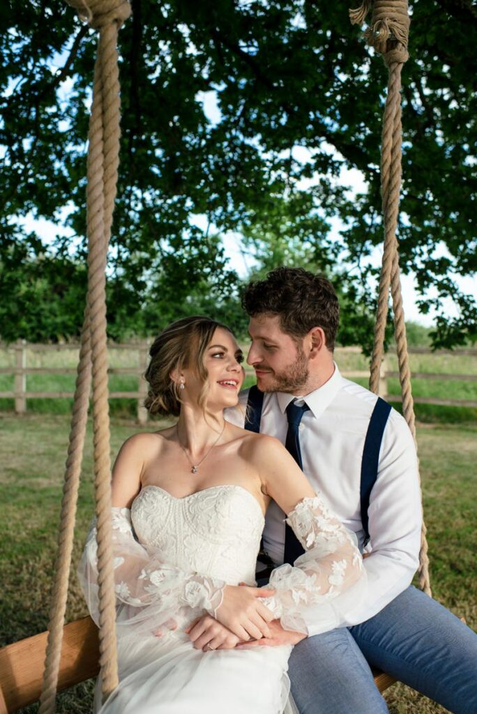 Bride and groom smile at each other on Milling Barn swing
