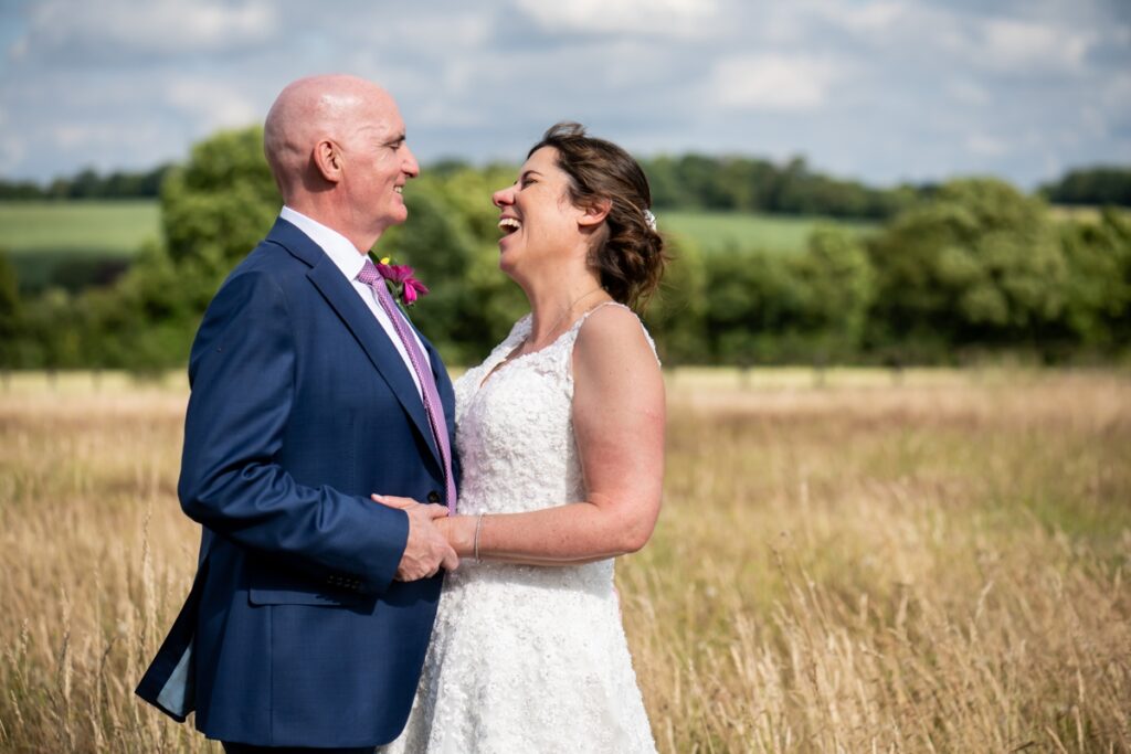 Bride and groom laugh in long grass at Beaumont Hall