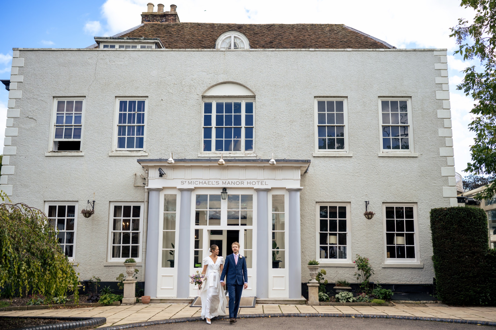 Bride and groom leave St Michael's Manor Hotel hand in hand in St Albans after their wedding ceremony