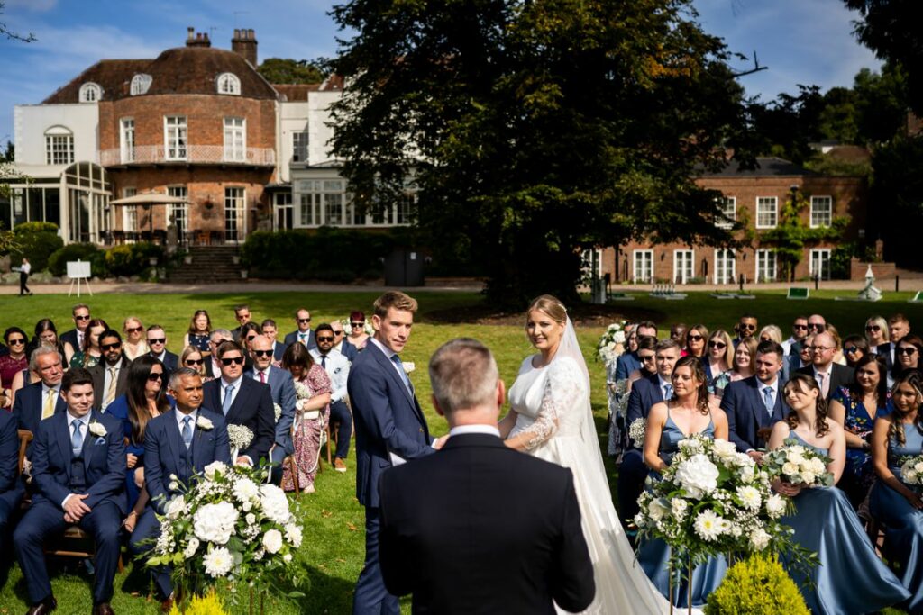 Sunny outdoor wedding ceremony with St Michaels Manor Hotel in St Albans in the background