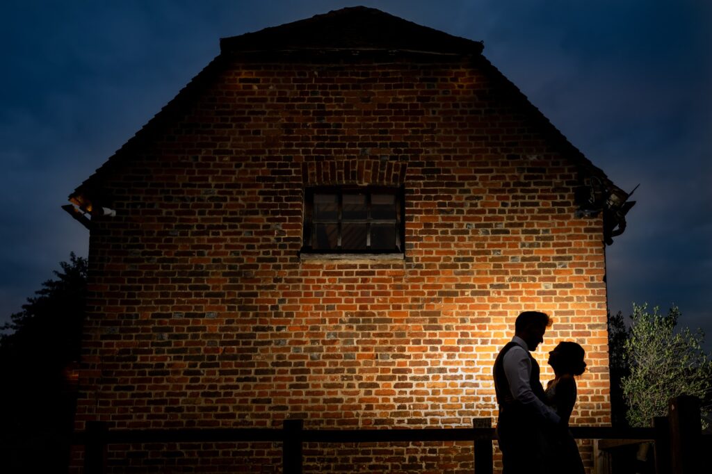 Bride and groom silhouetted against barn at Tewinbury Farm during blue hour