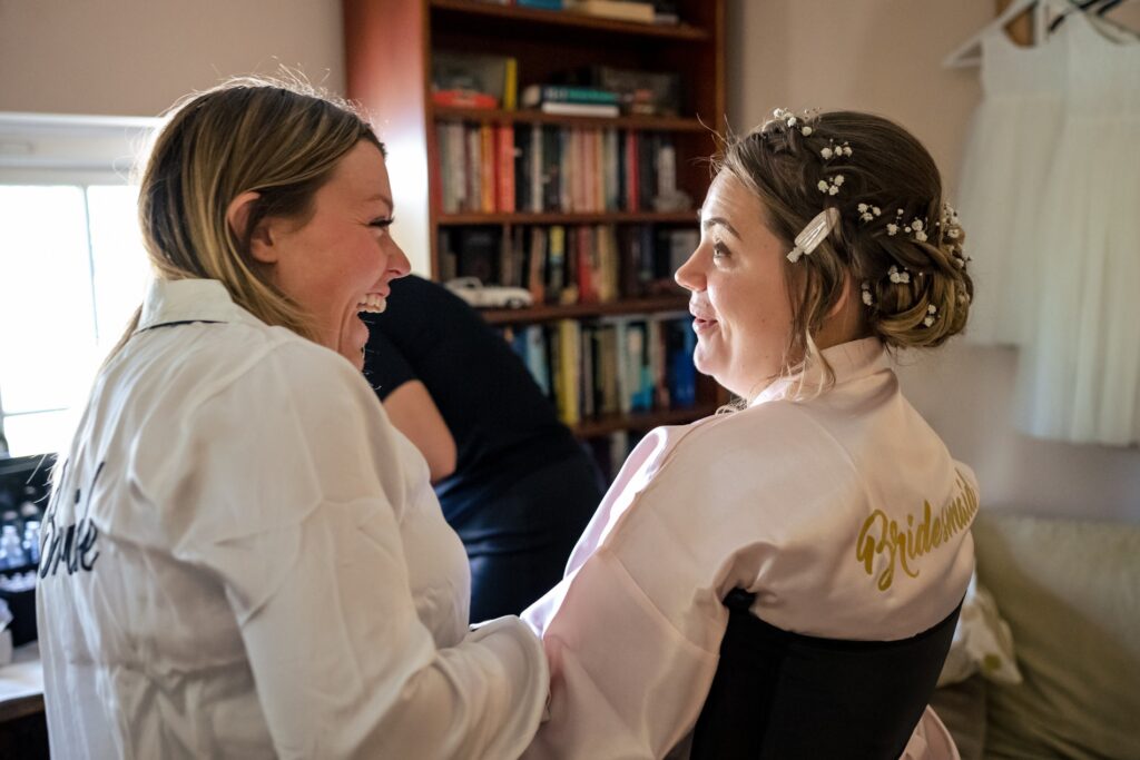 bride and bridesmaid laugh during makeup