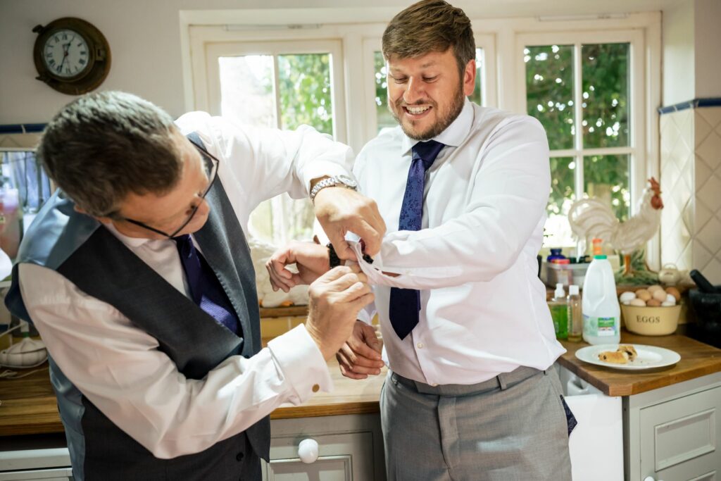 Dad helps groom with cufflinks in home kitchen