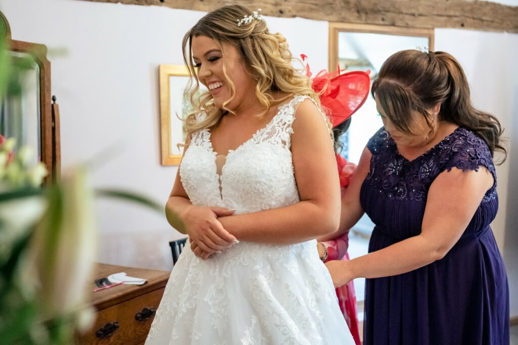 Bride laughs while sister and mum do up her dress