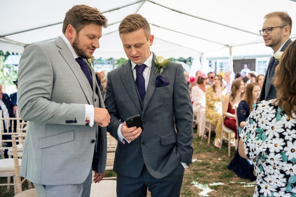 Groom and groomsman await bride while checking time