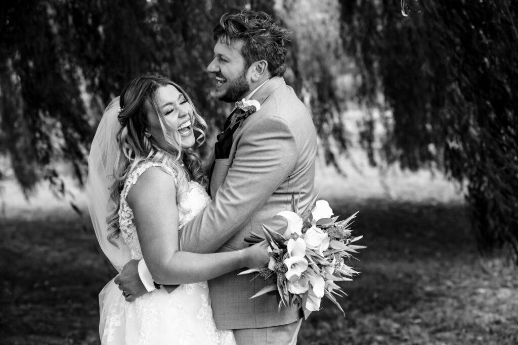 Bride and groom laugh in front of weeping willow