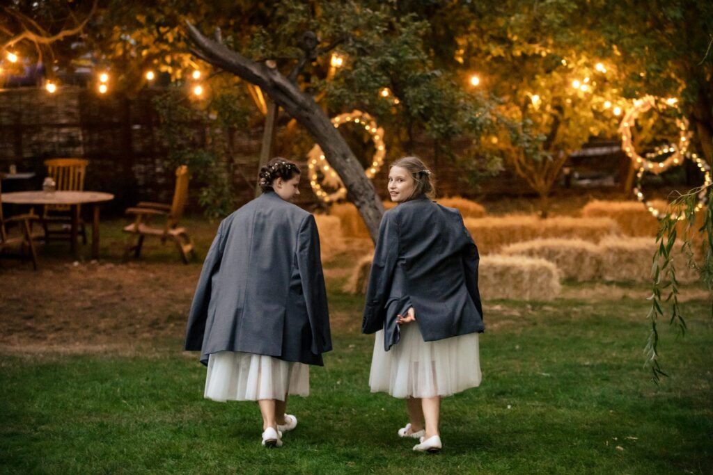 bridesmaids wearing suit jackets walk across fairy lit garden