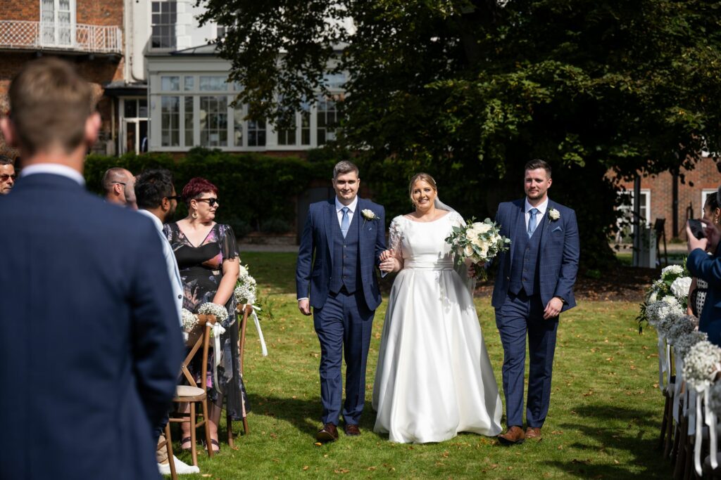 Bride walks down the outdoor aisle at St Michaels Manor wedding towards groom
