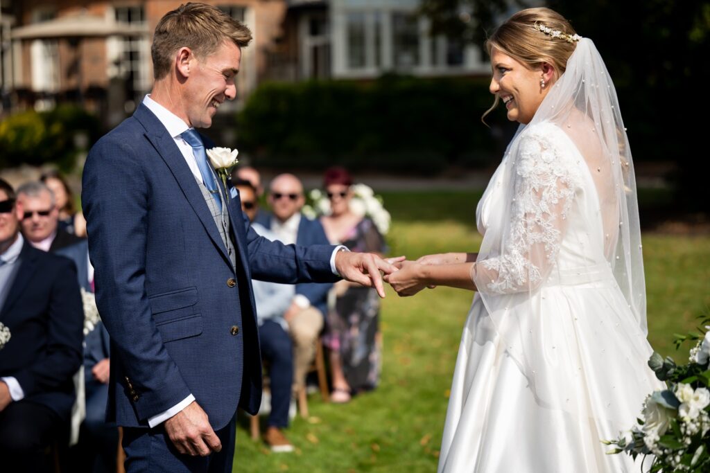 Bride slips ring onto grooms finger at St Michaels Manor outdoor wedding ceremony