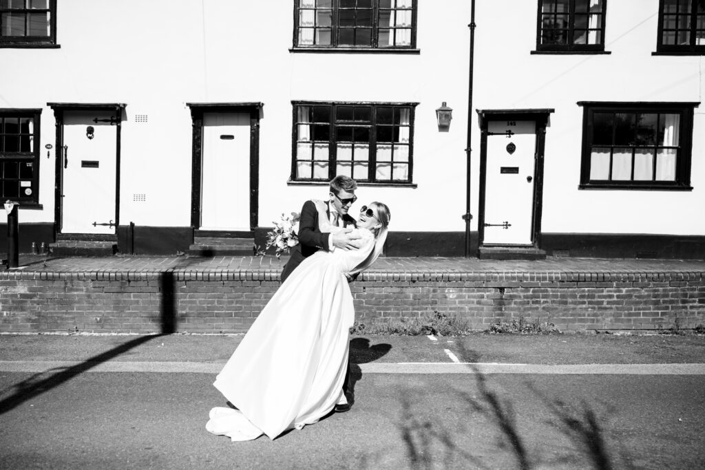 Bride and groom wearing sunglasses and dip kiss during couple portraits on Fishpool Street in St Albans