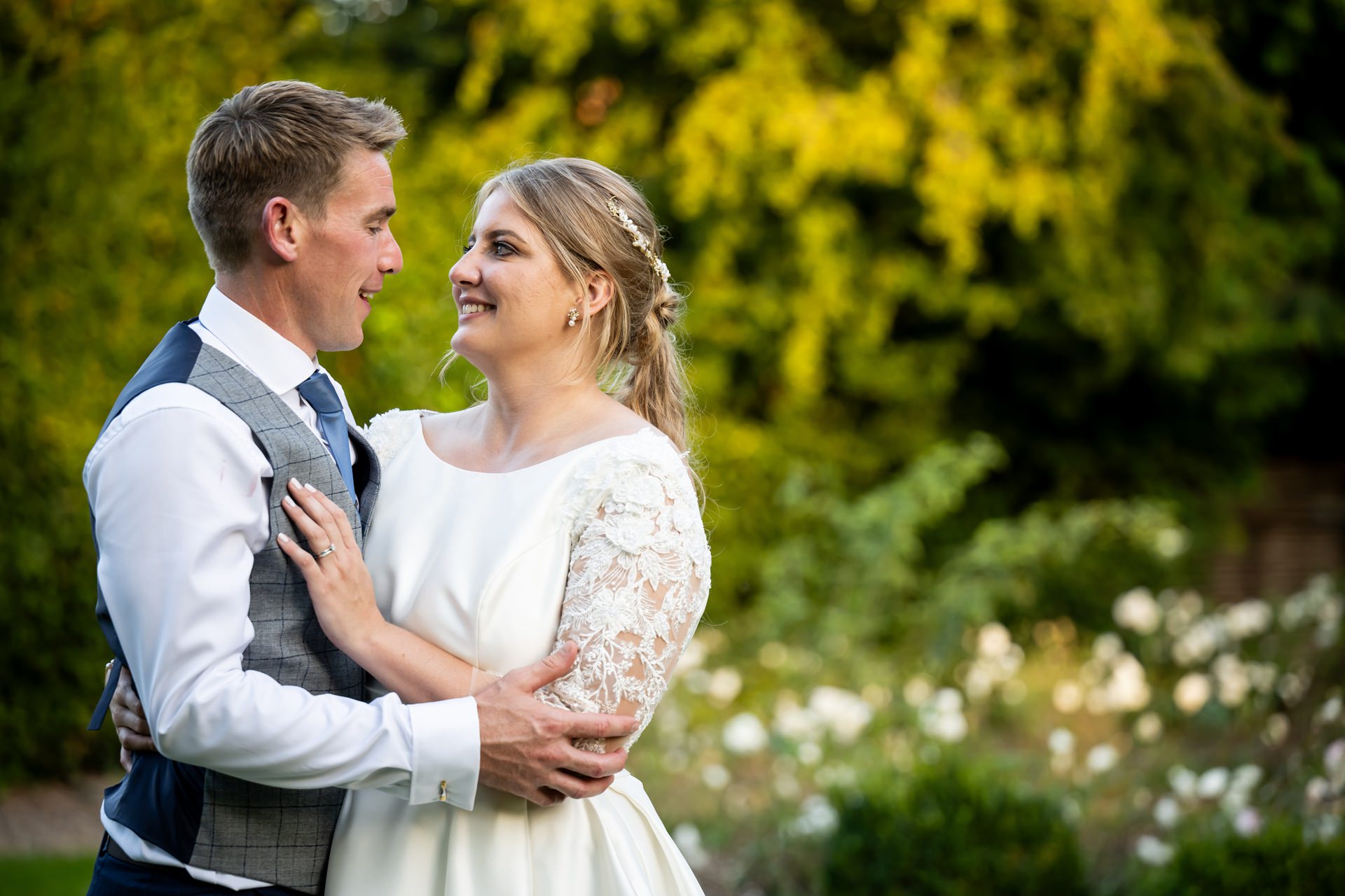 Bride and groom hug in front of summer flowers in St Michaels Manor gardens