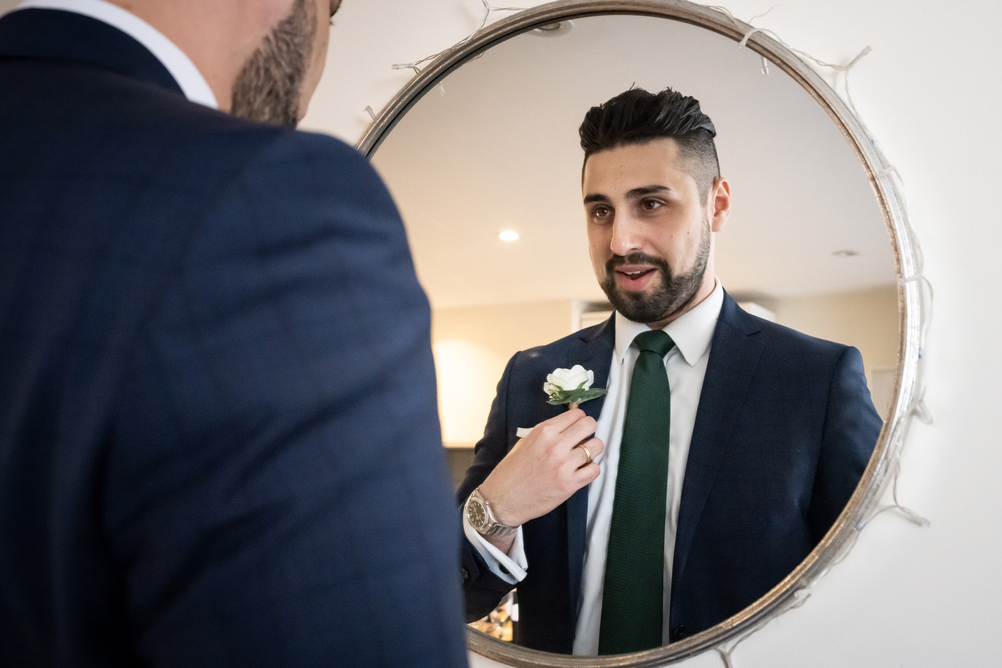 Groomsman puts on buttonhole in round mirror