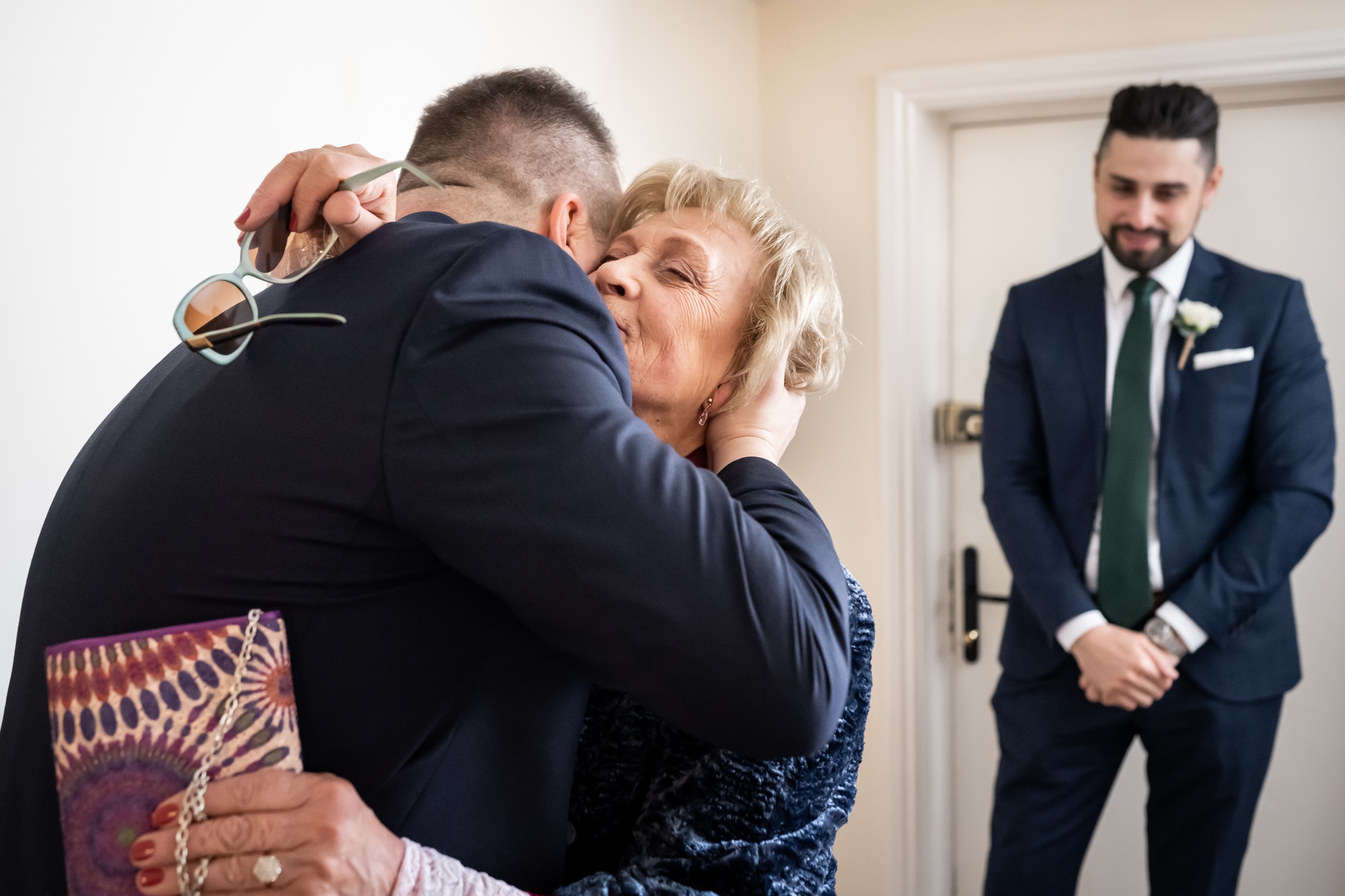 Groom greets mother with groomsman in the background