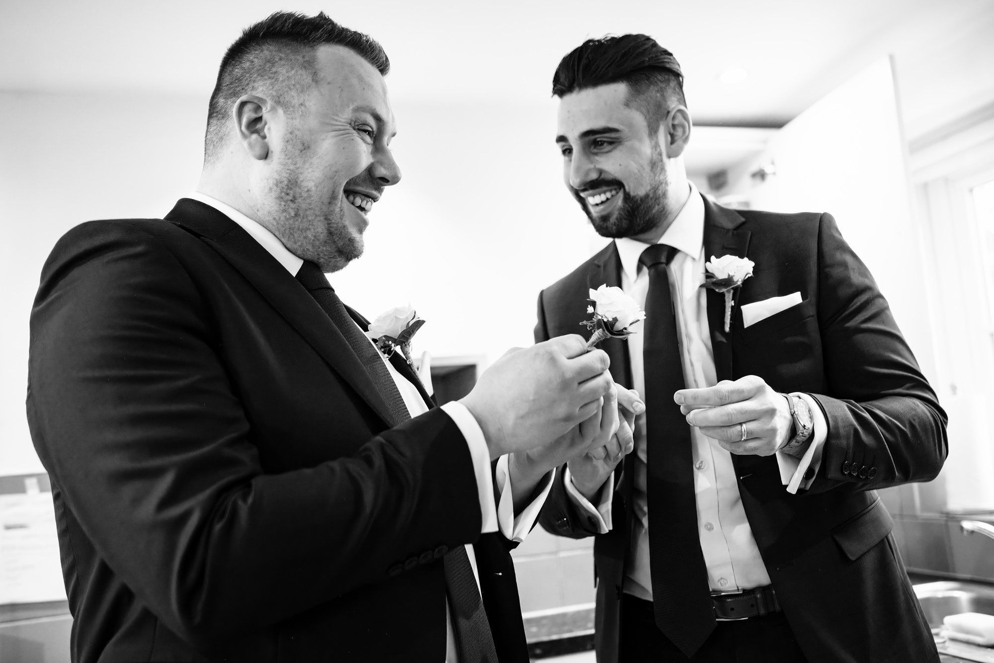 Groom and groomsman laugh trying to put on buttonholes