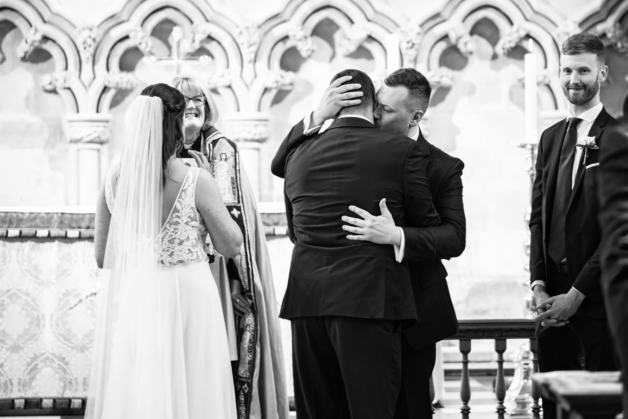 Groom kisses father of bride after he walks down the aisle of st albans cathedral