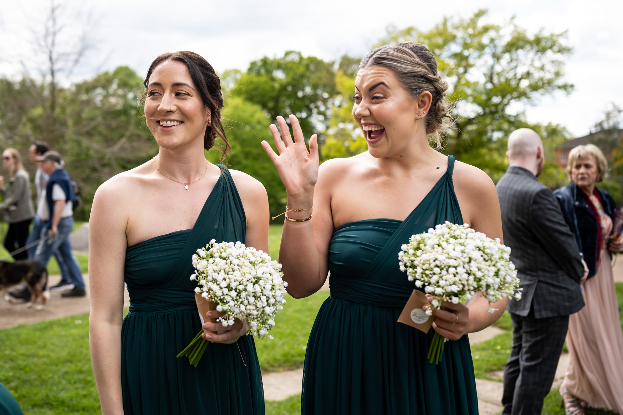 Bridesmaids in dark green dresses wave at wedding guests