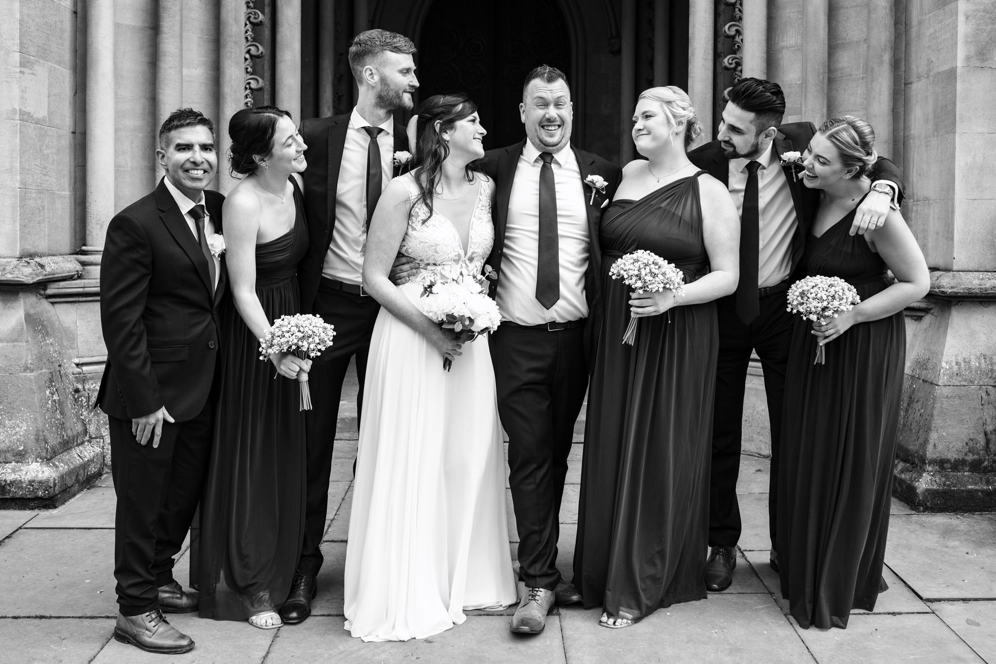Bride, groom and wedding party pose for formal portraits and laugh in front of St Albans Cathedral