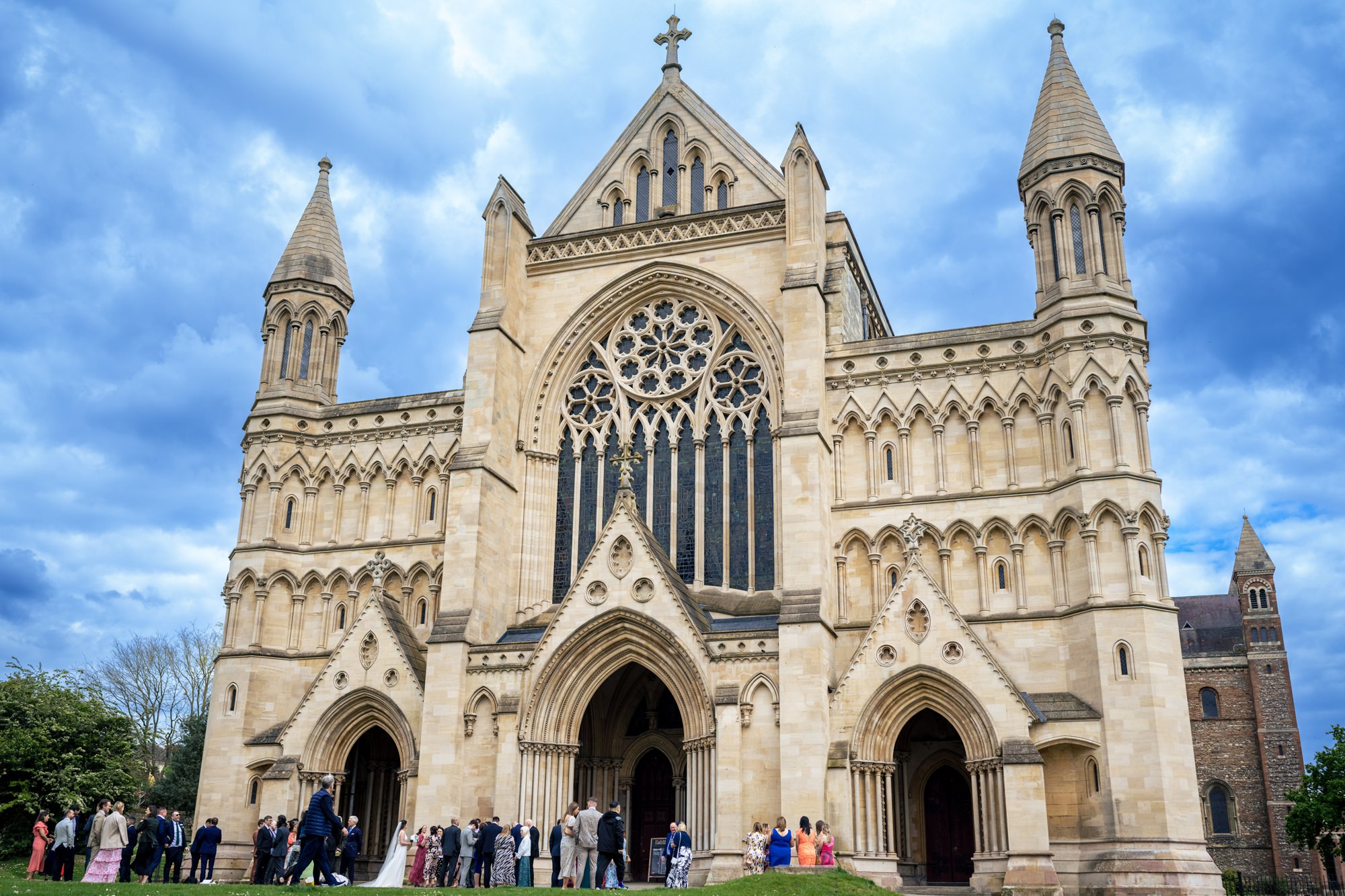 Wedding guests mingle in front of St Albans Cathedral after wedding ceremony