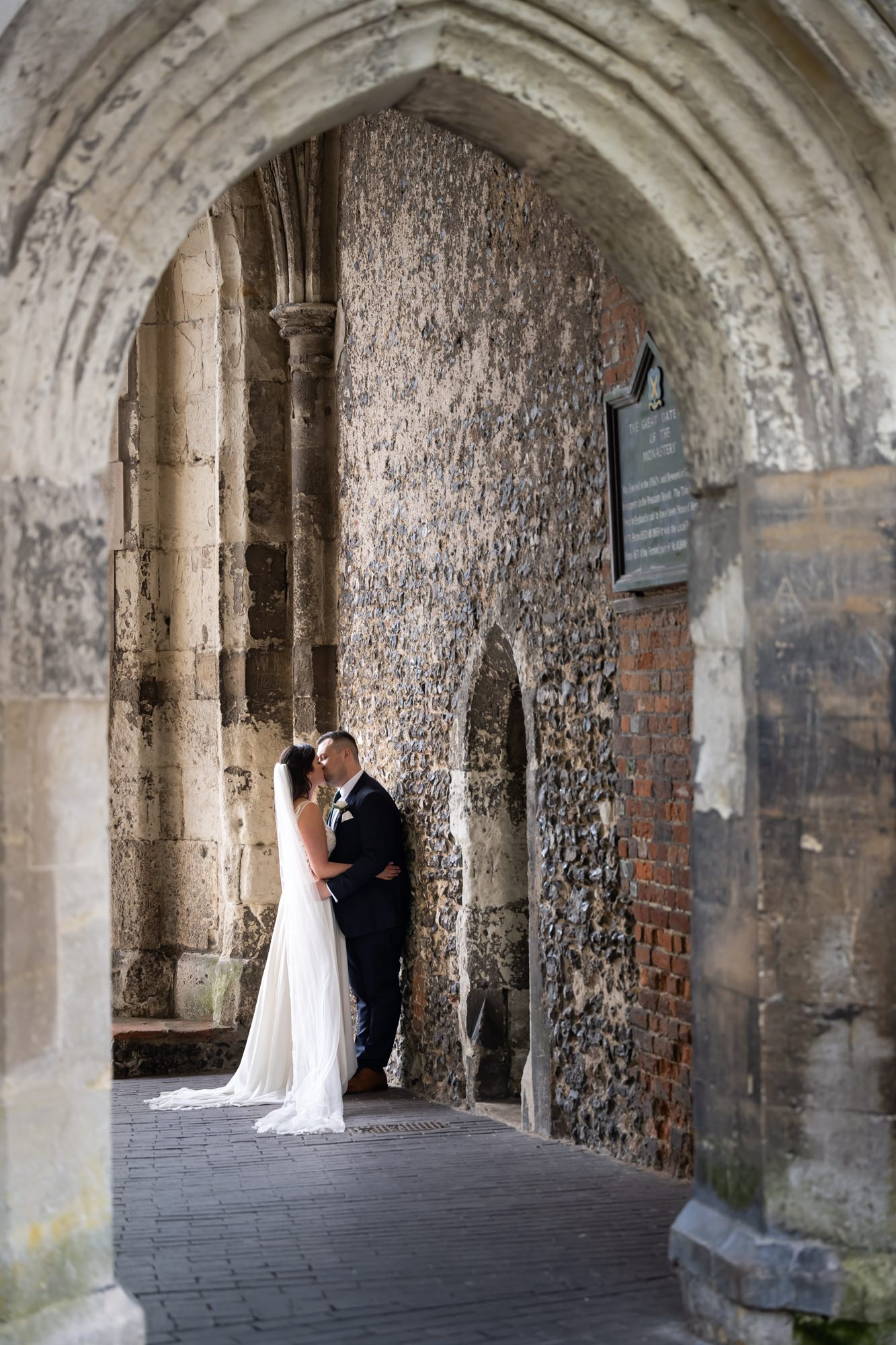 Bride and groom kiss in building arch after St Albans Cathedral wedding ceremony