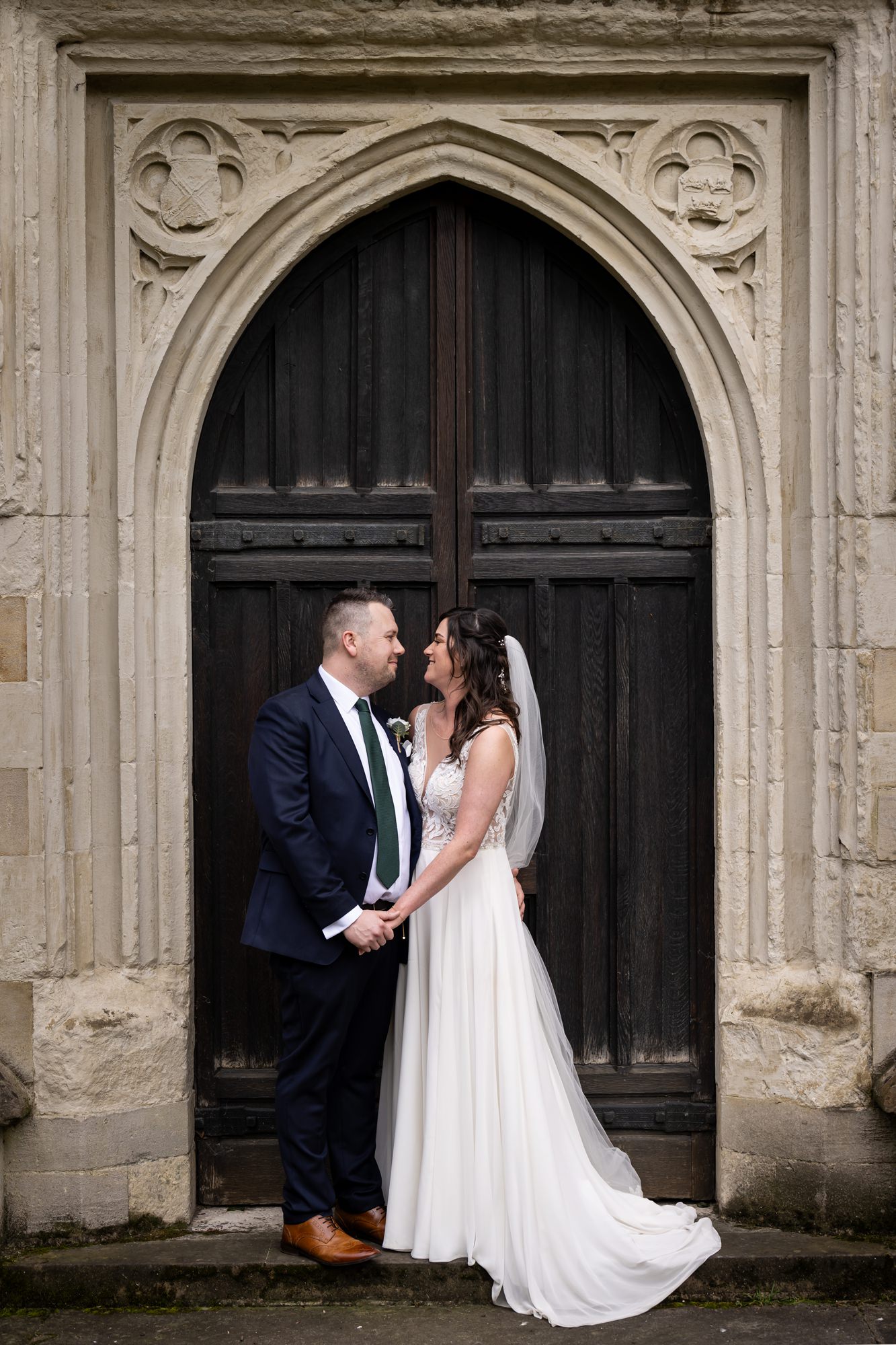Couple look at each other and smile in full length photo in doors of St Albans cathedral, Hertfordshire