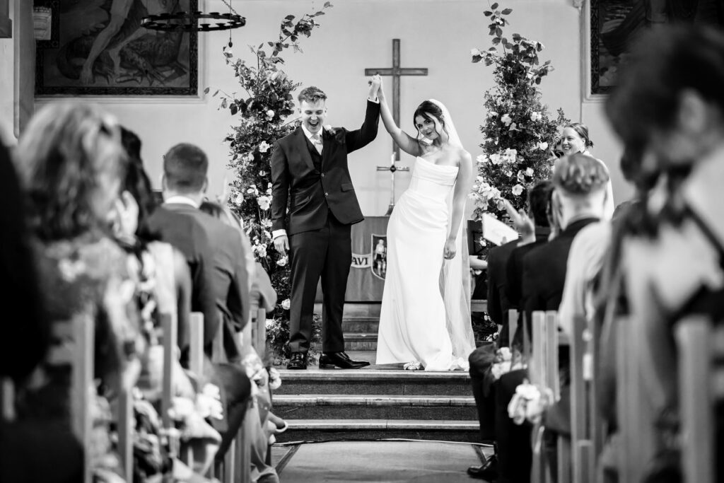 Bride and groom raise arms in celebration after being pronounced married during church wedding in Harpenden