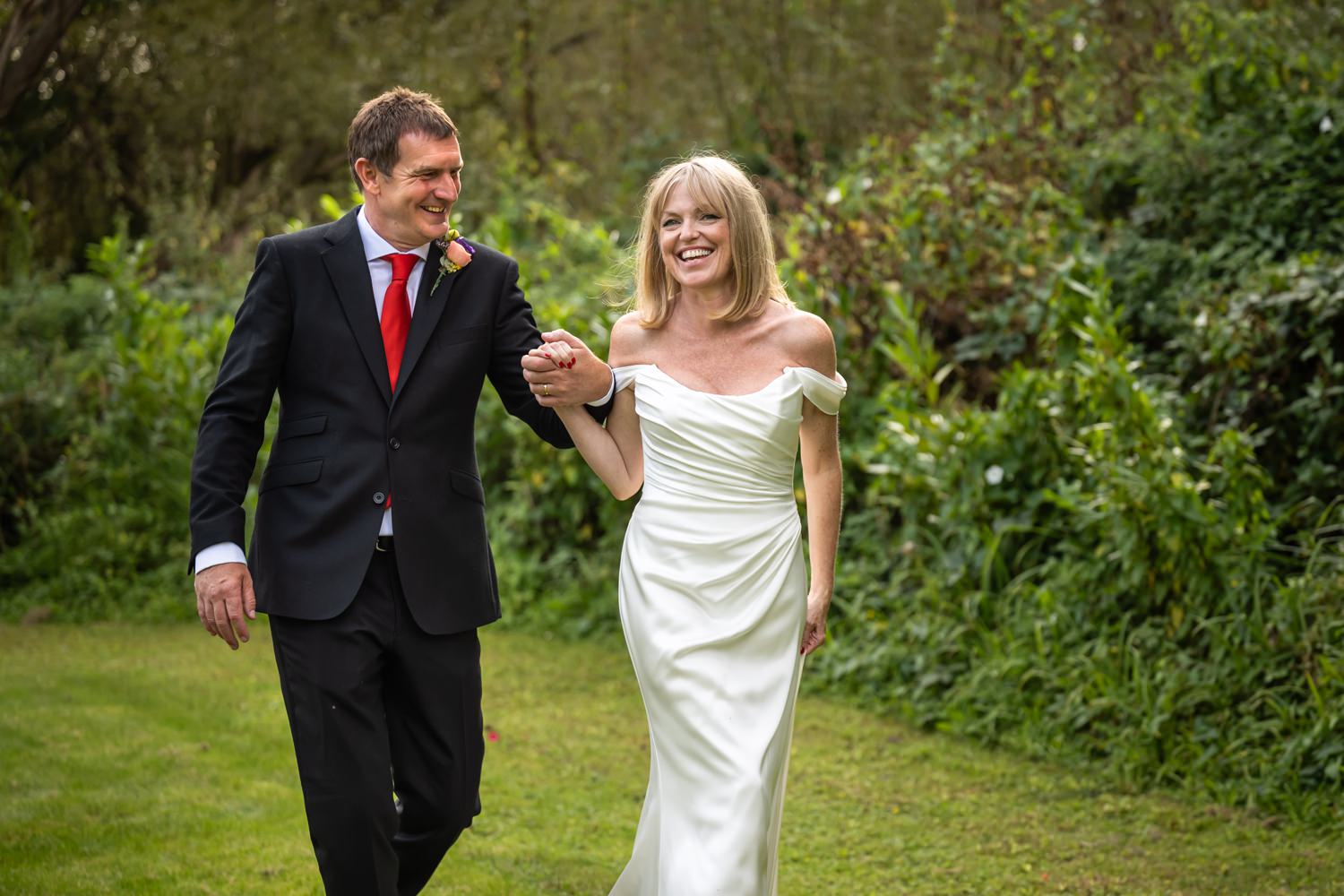 Bride and groom laugh and walk through grounds of Riverside Venue after intimate wedding ceremony