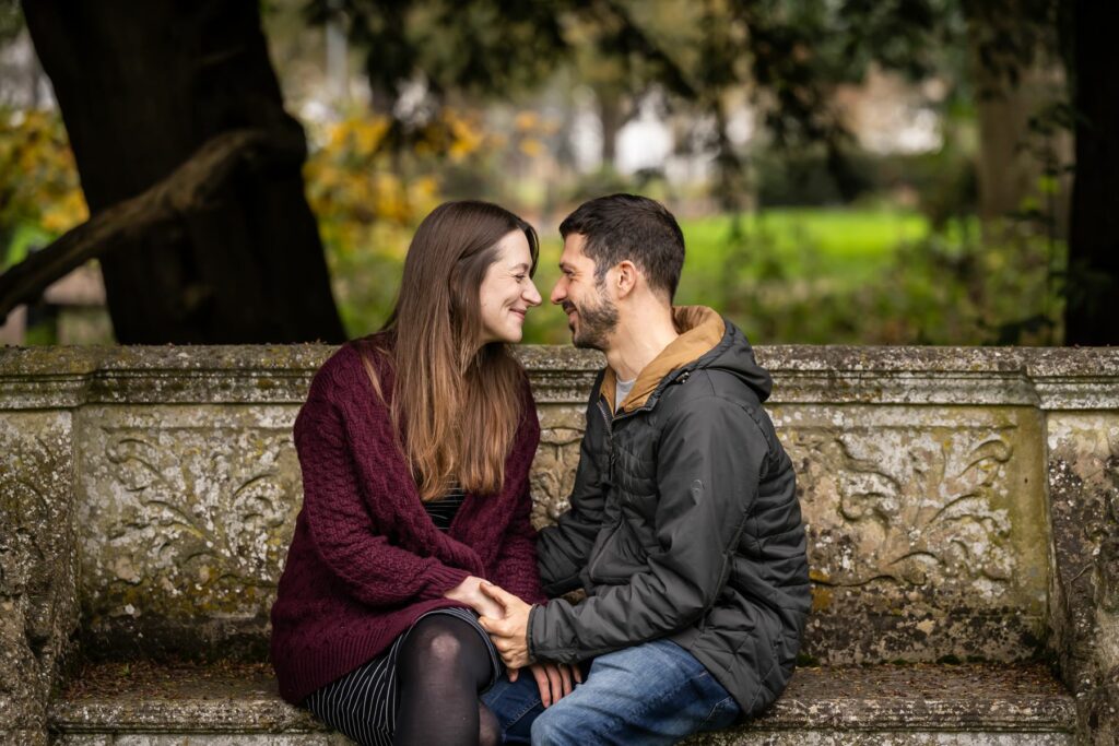 Couple sit on stone bench at Rothamsted Manor smiling at each other during engagement shoot