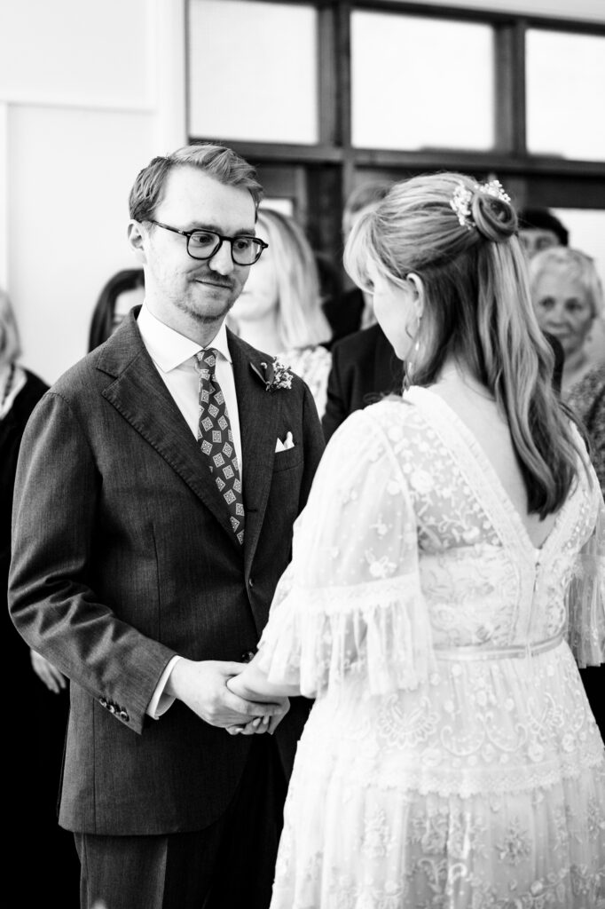 Groom holds brides hands during vows at during Hertford Register office intimate wedding in black and white photo