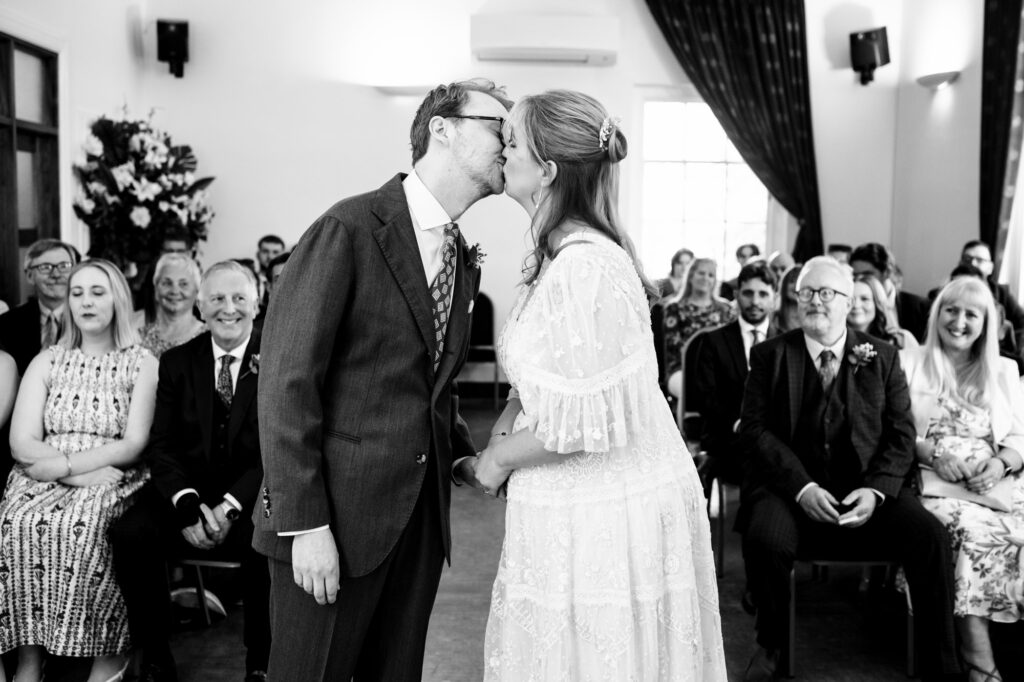 Bride and groom share first kiss during Hertford Register office intimate wedding in black and white photo
