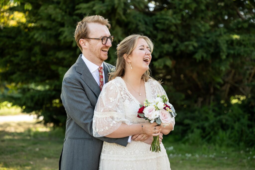 Bride and groom laugh in Hertford Register office gardens for relaxed couple portraits