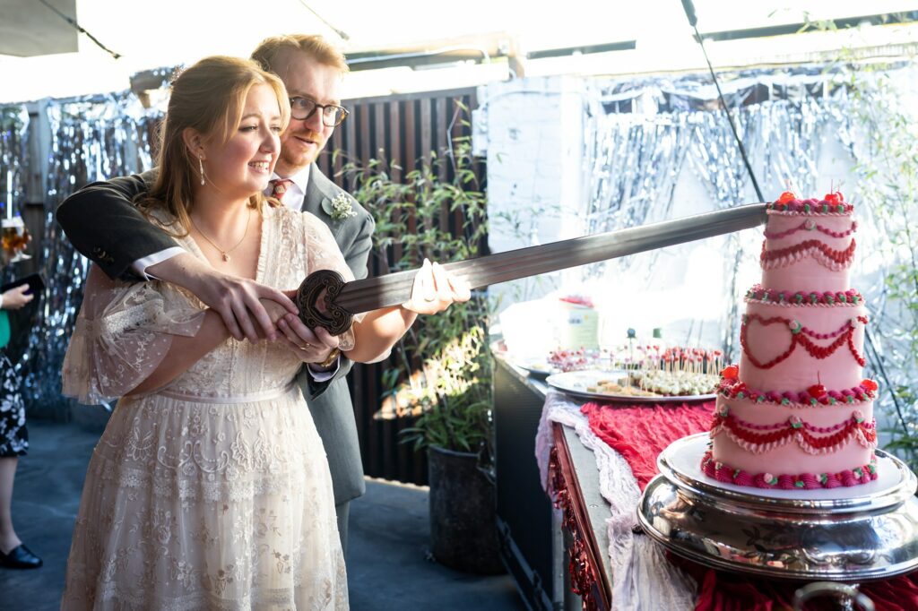 Bride and groom cut Lambeth style pink wedding cake with Lord of the Rings sword at pub reception wedding