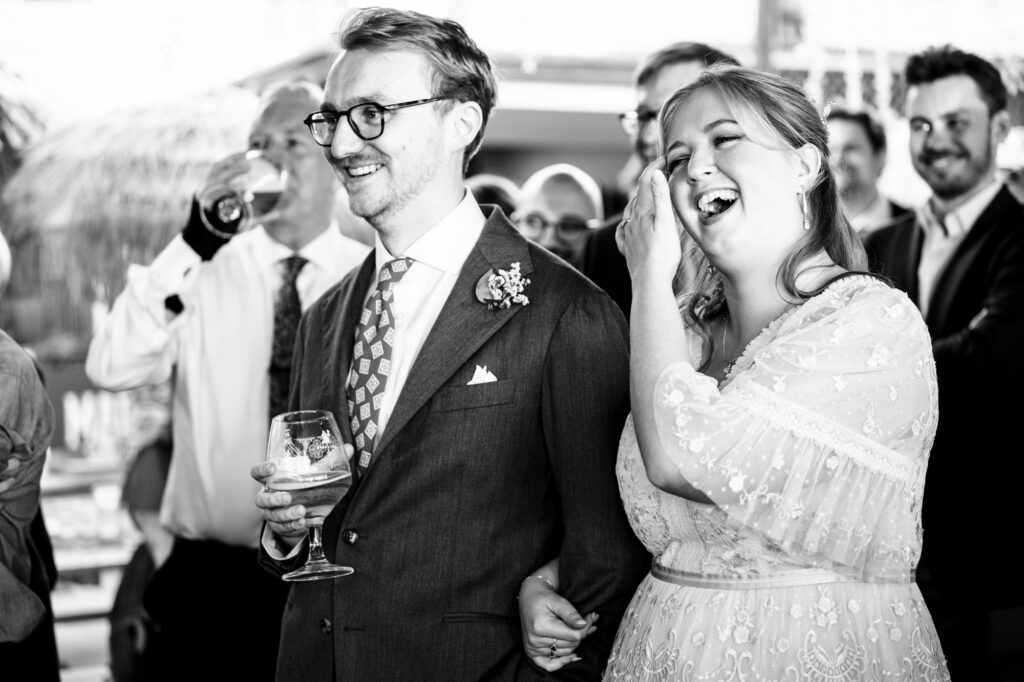 Bride and groom laugh during relaxed standing speeches at pub wedding reception