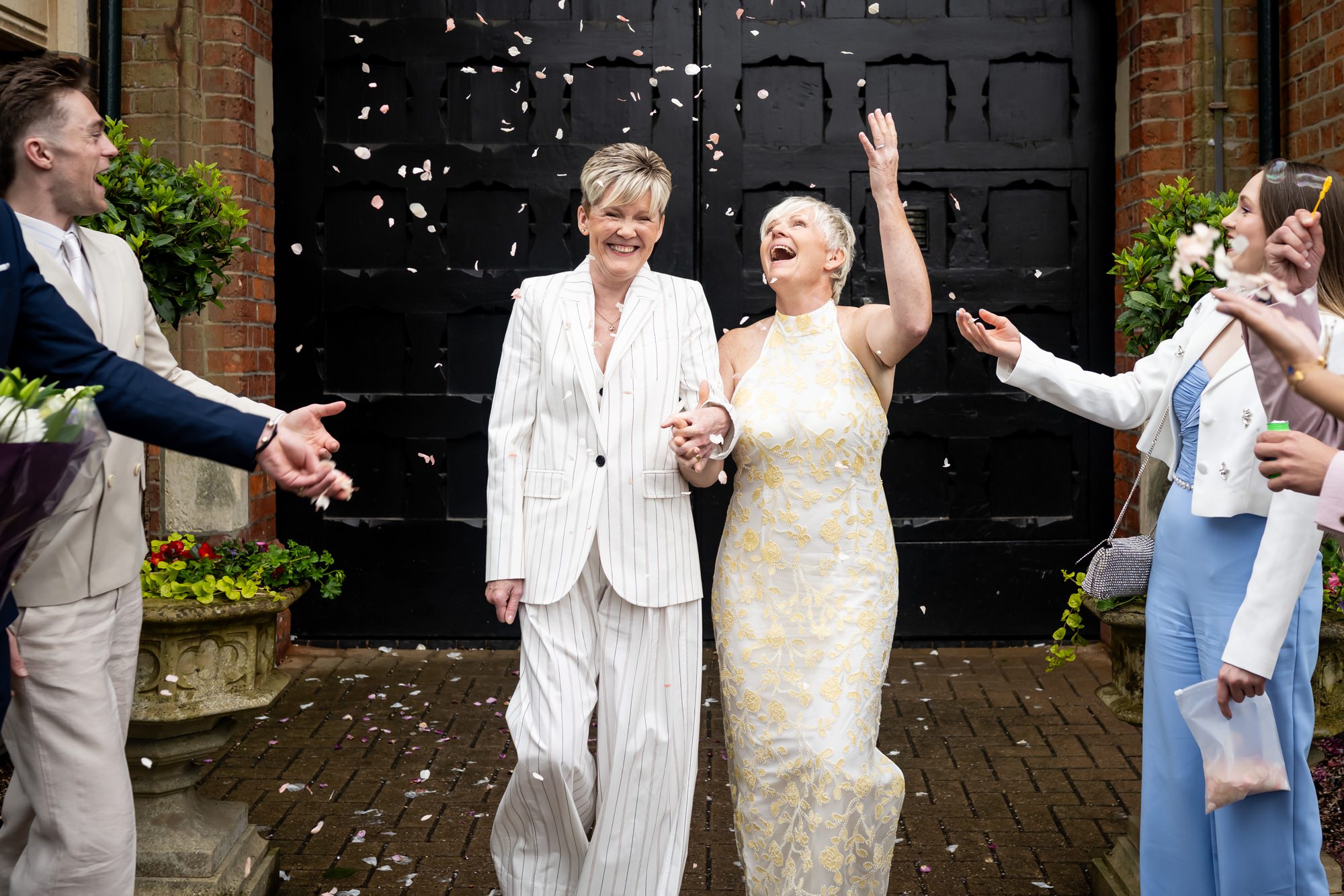 Bride in white suit and bride in white dress exit St Albans Gatehouse after civil partnership ceremony at Register Office