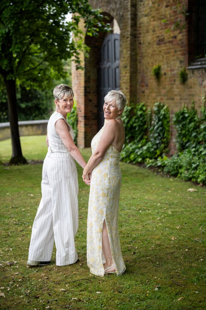 Two brides laugh for the camera during couple photos in St Albans Register Office gardens after micro wedding