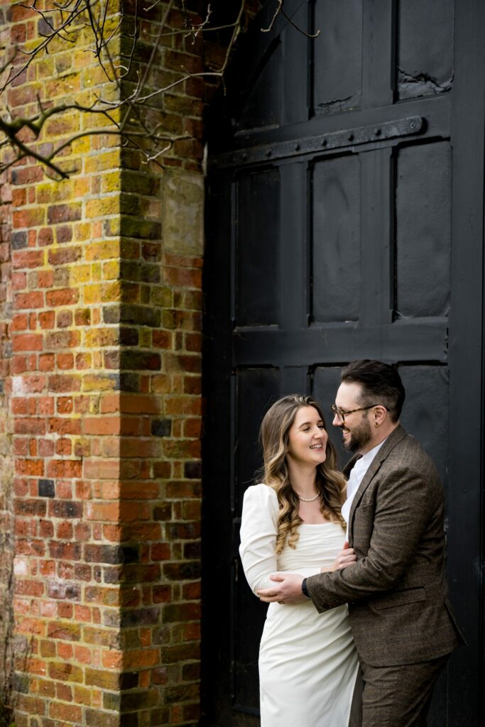 Bride and groom at micro winter wedding hug under bare trees in front of famous St Albans Register office black doors
