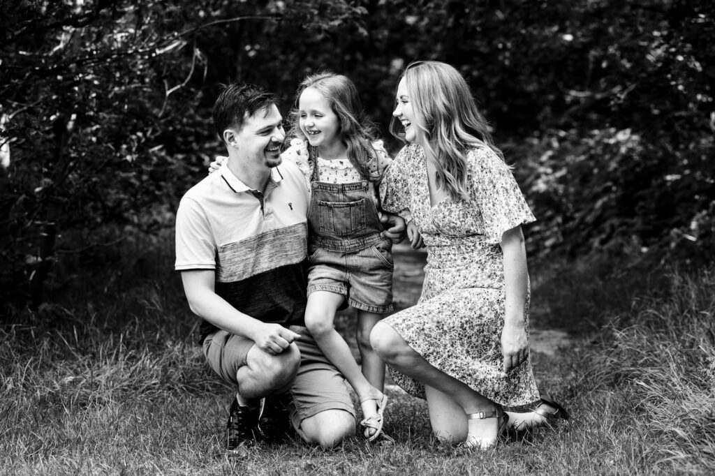 Family of three with daughter hug and laugh in black and white photo during family photos in St Albans