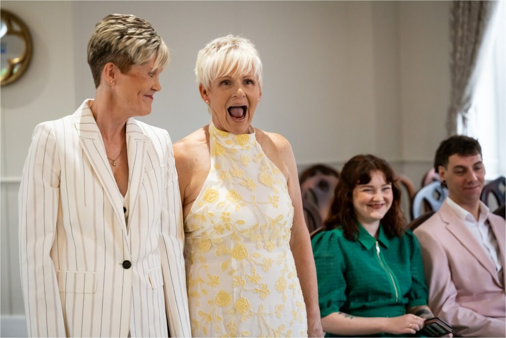Bride in white patterned dress looks shocked by words in civil partnership vows.