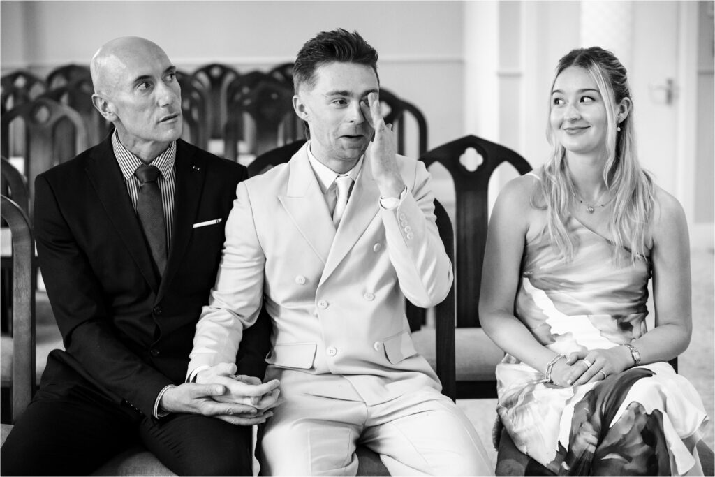 Bride's son wipes away tears while his sister smiles and looks on and he holds hands with his husband.