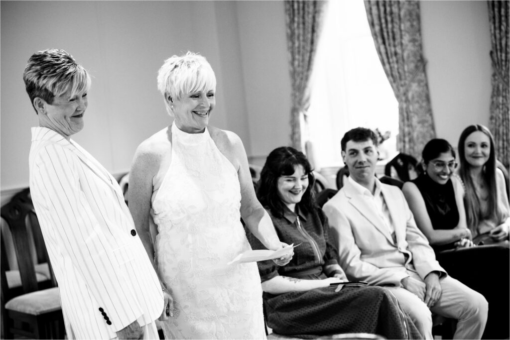 Two brides laugh while reading their personalised vows during an intimate civil partnership ceremony in St Albans.