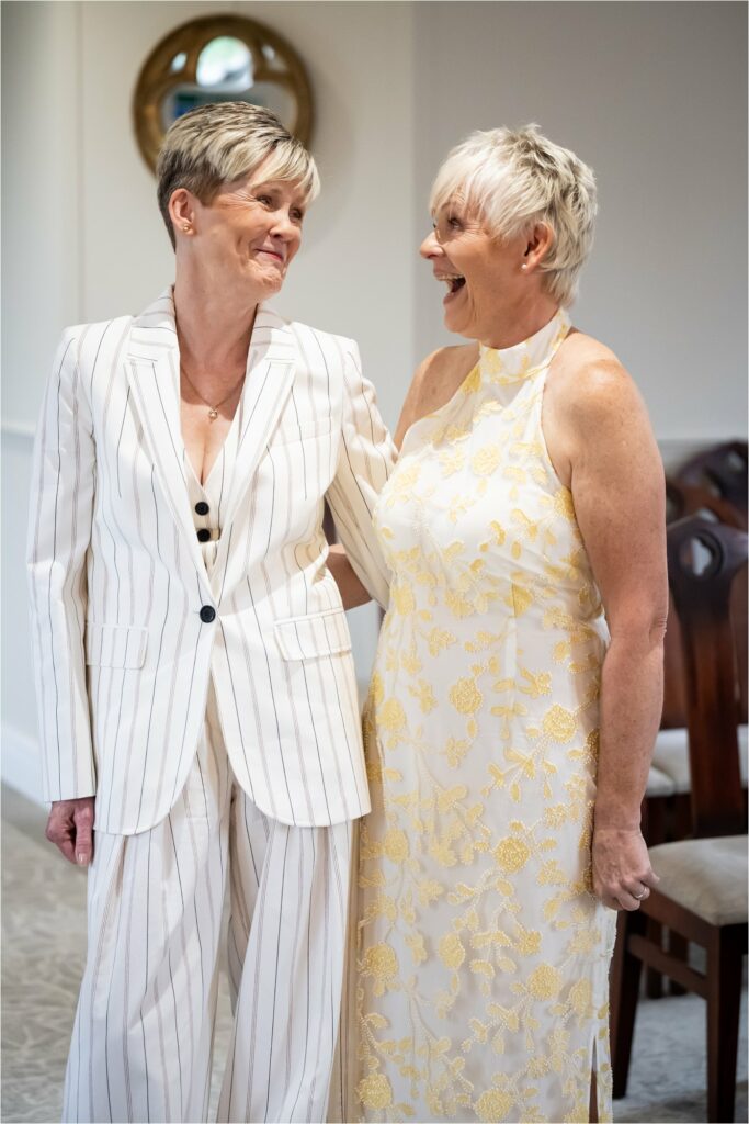 Two brides look at each other at laugh at content of wedding readings.