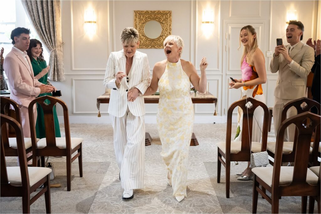 Brides dance down the aisle to S Club 7 to leave register office civil partnership ceremony, cheered on by guests.
