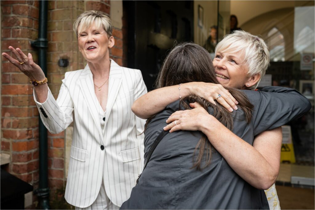 Bride hugs friend as new wife looks on and laughs with friends out of shot.
