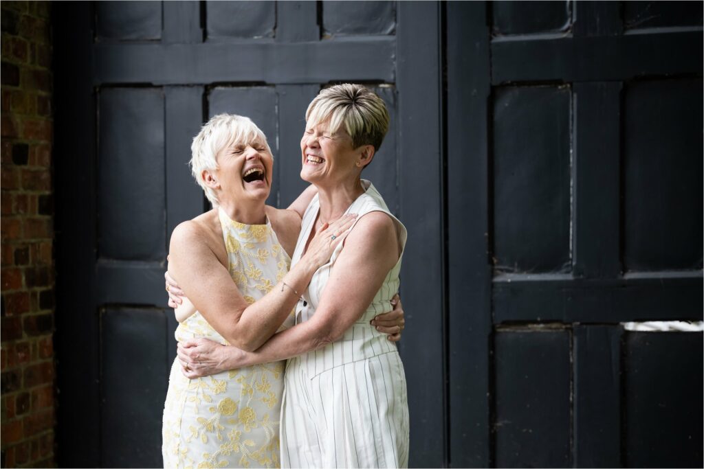 Two brides laugh hysterically with their eyes shut, holding each other in a tight embrace.