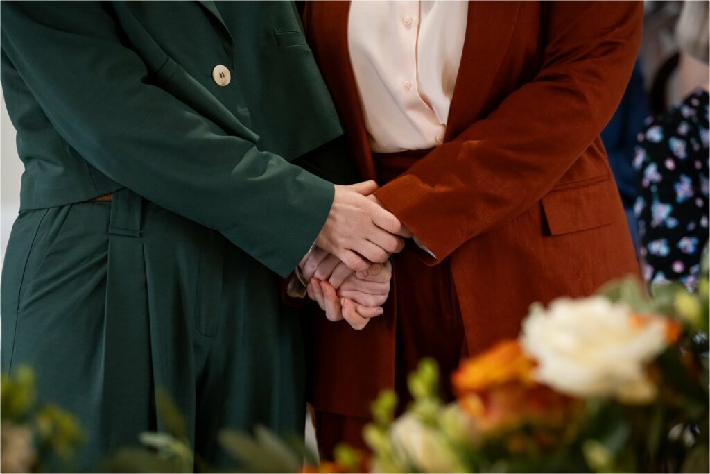 Two suit-wearing brides hold hands during their civil ceremony wedding.