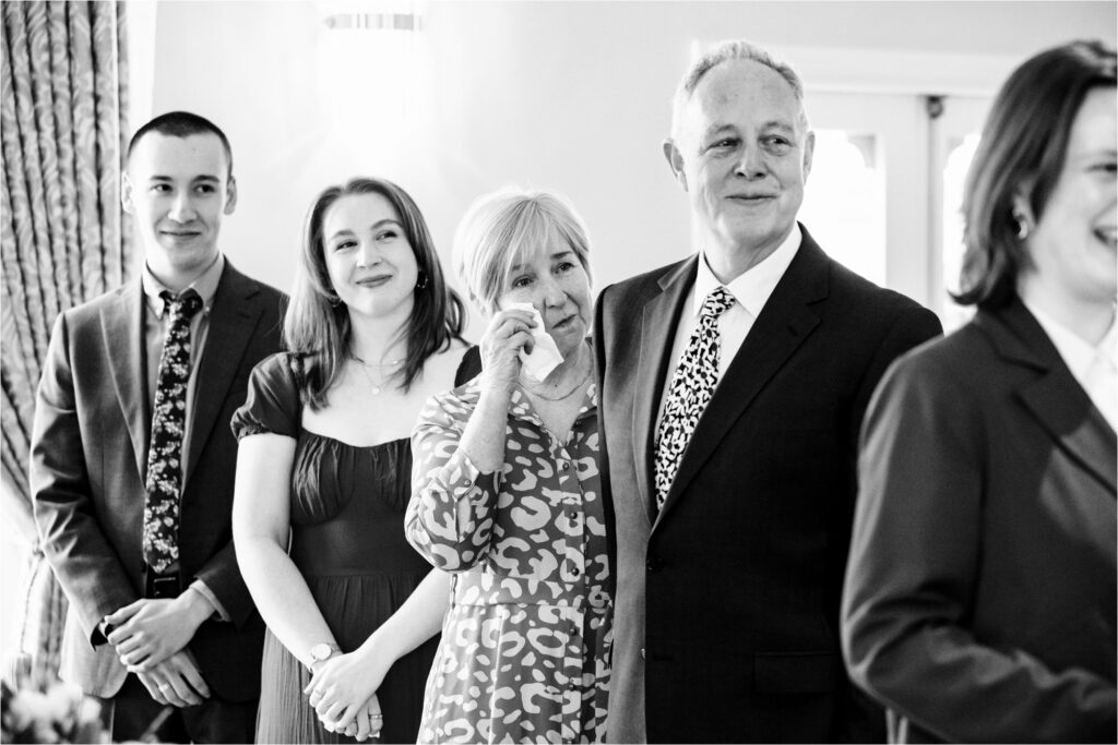 Emotional family members look on and smile or wipe away tears during wedding ceremony.