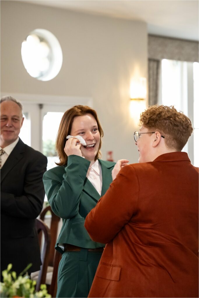 Two suit-wearing brides laugh and wipe away tears during emotional wedding vows