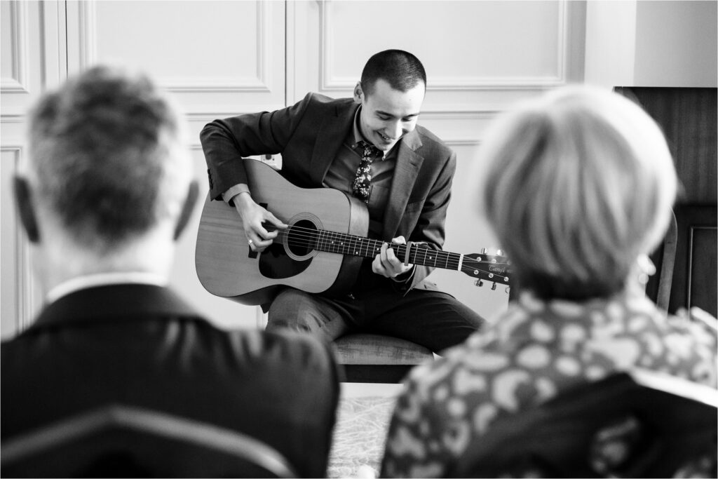 A family member plays guitar during intimate wedding ceremony paperwork signing.
