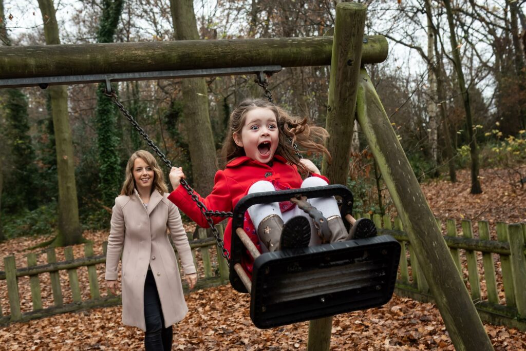 Little girl in red coat squealing with delight on swing in Hertfordshire park